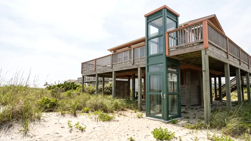 An outdoor home elevator tower with clear panels beside a raised coastal house